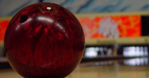 Close up of a dark red pattern bowling ball with bowling lanes and pins in the background, Wichita, KS