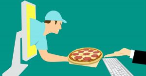 An illustration of online food delivery in Wichita, KS, with a delivery man reaching through the computer offering a pizza to a customer's outstretched hand.